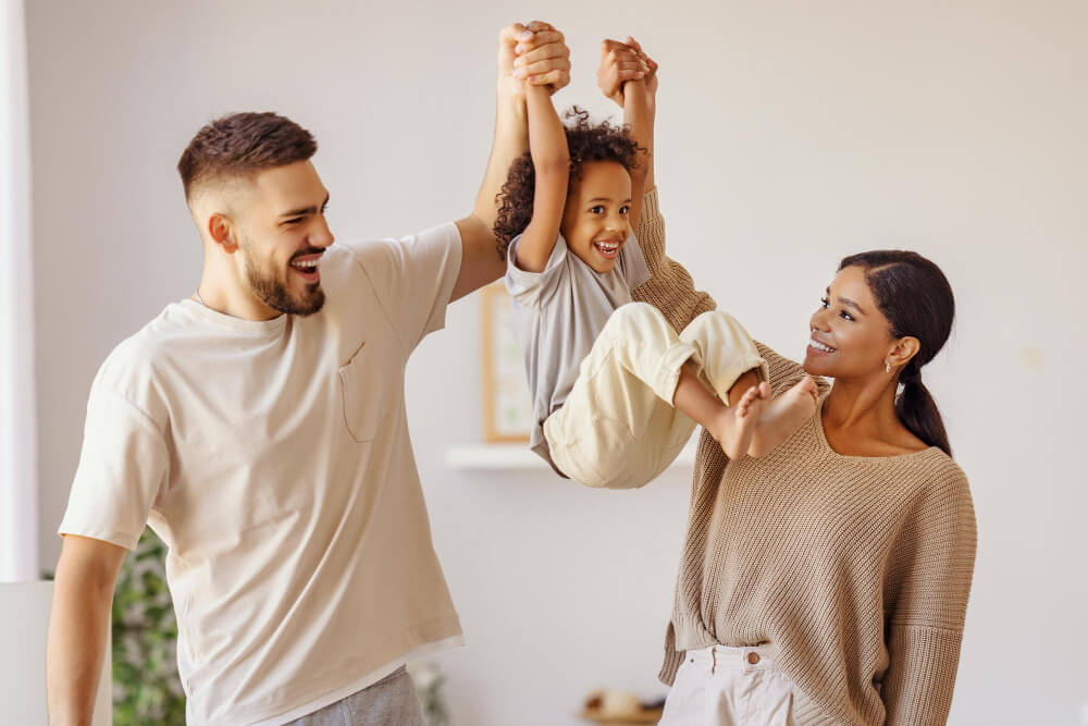 Full body multiethnic father and mother smiling and lifting mixed race son in cozy living room